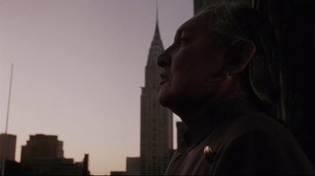 Movie still from “Insignificance” (1985), directed by Nicolas Roeg – A man standing in front of a building with a building in the background; Close Up shot, Low angle