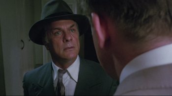 Movie still from “Insignificance” (1985), directed by Nicolas Roeg – A man wearing a suit and hat looking at himself in the mirror; Close Up shot, Over the shoulder angle