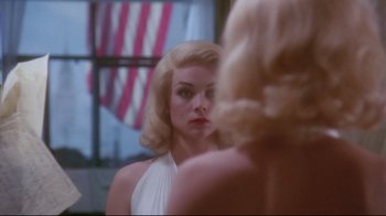 Movie still from “Insignificance” (1985), directed by Nicolas Roeg – A woman looking into a mirror in front of a window; Close Up shot, Over the shoulder angle