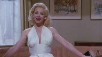 Movie still from “Insignificance” (1985), directed by Nicolas Roeg – A woman in a white dress standing in front of a pink couch; Medium shot, Low angle