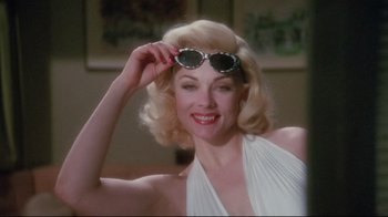 Movie still from “Insignificance” (1985), directed by Nicolas Roeg – A woman in a white dress holding a pair of sunglasses; Close Up shot, Low angle