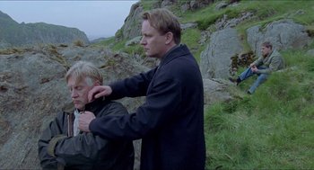 Movie still from “Insomnia” (1997), directed by Erik Skjoldbjærg – A man is helping another man with his jacket; Medium shot, Over the shoulder angle