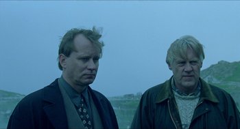 Movie still from “Insomnia” (1997), directed by Erik Skjoldbjærg – Two men standing next to each other on a field; Medium shot, Low angle