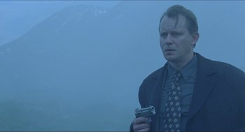 Movie still from “Insomnia” (1997), directed by Erik Skjoldbjærg – A man holding a camera in the fog with mountains in the background; Medium shot, Low angle