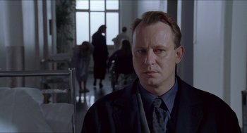 Movie still from “Insomnia” (1997), directed by Erik Skjoldbjærg – A man wearing a suit and tie standing in front of people; Close Up shot, Over the shoulder angle