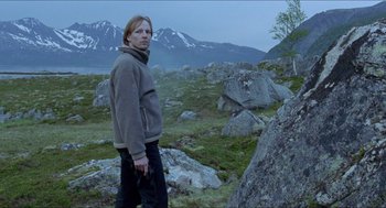 Movie still from “Insomnia” (1997), directed by Erik Skjoldbjærg – A person standing in a field with a mountain in the background; Medium shot, Low angle