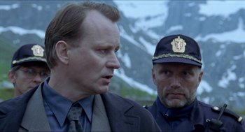 Movie still from “Insomnia” (1997), directed by Erik Skjoldbjærg – A man in a suit standing next to another man in a uniform; Close Up shot, Over the shoulder angle