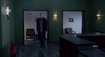 Movie still from “Insomnia” (1997), directed by Erik Skjoldbjærg – A man standing in a room with a chair and a table; Wide shot, Low angle