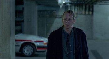 Movie still from “Insomnia” (1997), directed by Erik Skjoldbjærg – A man standing in front of a car in a parking lot; Medium shot, Over the shoulder angle