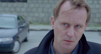Movie still from “Insomnia” (1997), directed by Erik Skjoldbjærg – A person wearing a jacket on the side of the road; Close Up shot, Over the shoulder angle