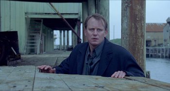 Movie still from “Insomnia” (1997), directed by Erik Skjoldbjærg – A man sitting at a table in front of a wooden structure; Medium shot, Low angle