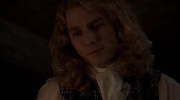 Movie still from “Interview with the Vampire: The Vampire Chronicles” (1994), directed by Neil Jordan – A man with long blonde curly hair wearing a vest; Close Up shot, Over the shoulder angle