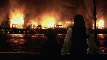 Movie still from “Interview with the Vampire: The Vampire Chronicles” (1994), directed by Neil Jordan – Two people sitting on a bench looking at a fire in the background; Extreme Wide shot, Over the shoulder angle