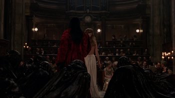 Movie still from “Interview with the Vampire: The Vampire Chronicles” (1994), directed by Neil Jordan – A woman in a long red dress standing in front of an audience; Wide shot, Over the shoulder angle