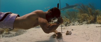 Movie still from “Into the Blue” (2005), directed by John Stockwell – A man is holding a stick in his mouth while looking at a shark; Wide shot, Low angle