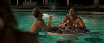 Movie still from “Into the Blue” (2005), directed by John Stockwell – Two men sitting in a swimming pool with drinks and a cigar; Medium shot, Over the shoulder angle