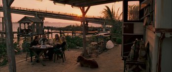 Movie still from “Into the Blue” (2005), directed by John Stockwell – Two people sitting at a table with a dog under an awning; Wide shot, Over the shoulder angle