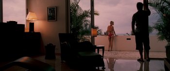Movie still from “Into the Blue” (2005), directed by John Stockwell – A woman in a pink bikini sitting on a chair in front of a window looking out at the ocean; Wide shot, Over the shoulder angle