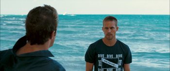 Movie still from “Into the Blue” (2005), directed by John Stockwell – A man standing next to another man on the beach; Close Up shot, Over the shoulder angle