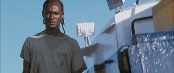 Movie still from “Into the Blue” (2005), directed by John Stockwell – A man standing in front of a building with a sign in the background; Close Up shot, Low angle