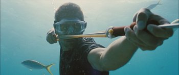 Movie still from “Into the Blue” (2005), directed by John Stockwell – A man in a black shirt is holding a stick underwater; Medium shot, High angle