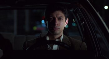 Movie still from “Into the Night” (1985), directed by John Landis – A man sitting in the drivers seat of a car at night; Close Up shot, Low angle