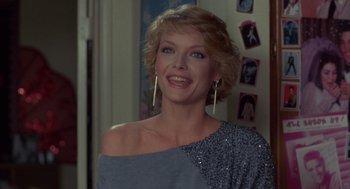 Movie still from “Into the Night” (1985), directed by John Landis – A woman in a blue top smiles for the camera; Close Up shot, Over the shoulder angle