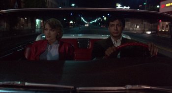 Movie still from “Into the Night” (1985), directed by John Landis – A man and a woman sitting in the back seat of a car; Wide shot, Low angle