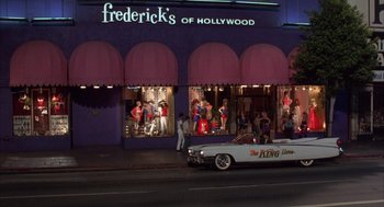 Movie still from “Into the Night” (1985), directed by John Landis – A car driving down a street next to a building; Extreme Wide shot, Low angle