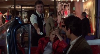 Movie still from “Into the Night” (1985), directed by John Landis – A woman in a red leather jacket holding a cell phone to her head; Medium shot, Over the shoulder angle