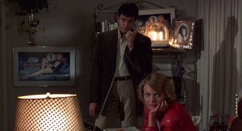 Movie still from “Into the Night” (1985), directed by John Landis – A man and a woman sitting at a table talking on the phone; Medium shot, Low angle