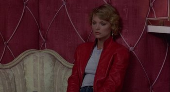 Movie still from “Into the Night” (1985), directed by John Landis – A woman in a red jacket sitting on a couch; Medium shot, High angle