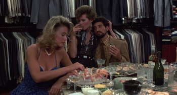 Movie still from “Into the Night” (1985), directed by John Landis – A group of people sitting around a table with food; Medium shot, Over the shoulder angle