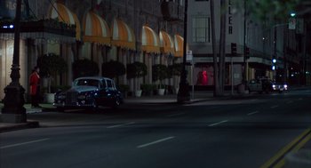 Movie still from “Into the Night” (1985), directed by John Landis – A car driving down a street at night past tall buildings; Extreme Wide shot, High angle