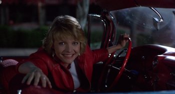 Movie still from “Into the Night” (1985), directed by John Landis – A woman sitting in the driver's seat of a car; Medium shot, Low angle