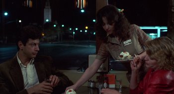 Movie still from “Into the Night” (1985), directed by John Landis – A woman serving a plate of cake at a restaurant; Medium shot, Over the shoulder angle