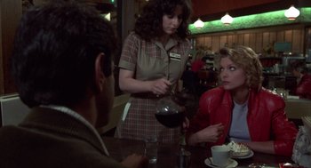 Movie still from “Into the Night” (1985), directed by John Landis – A woman pouring a drink into a cup at a restaurant; Medium shot, Over the shoulder angle