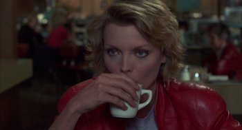 Movie still from “Into the Night” (1985), directed by John Landis – A woman is drinking a cup of coffee; Close Up shot, Over the shoulder angle