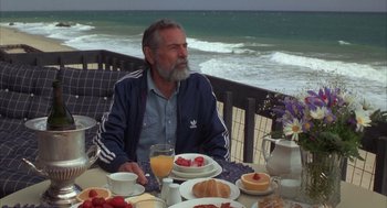 Movie still from “Into the Night” (1985), directed by John Landis – An older man sitting at a table with a plate of food; Medium shot, Low angle