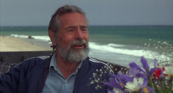 Movie still from “Into the Night” (1985), directed by John Landis – An older man sitting on a bench near the ocean; Close Up shot, Over the shoulder angle
