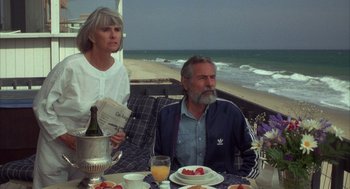Movie still from “Into the Night” (1985), directed by John Landis – An older man and woman sitting at an outdoor table; Medium shot, High angle