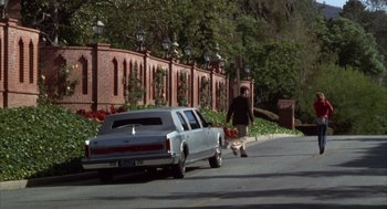 Movie still from “Into the Night” (1985), directed by John Landis – A man walking down the street near a car; Wide shot, Over the shoulder angle