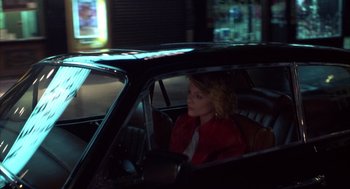 Movie still from “Into the Night” (1985), directed by John Landis – A woman sitting in the driver's seat of a car at night; Wide shot, High angle
