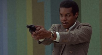 Movie still from “Into the Night” (1985), directed by John Landis – A man in a suit and tie holding a gun in his hand; Close Up shot, Low angle