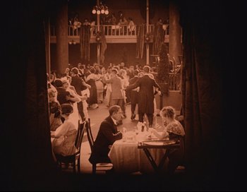 Movie still from “Intolerance” (1916), directed by D.W. Griffith – A group of people sitting at tables in a room; Extreme Wide shot, High angle
