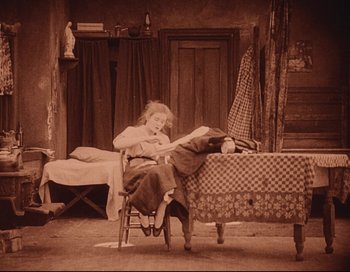 Movie still from “Intolerance” (1916), directed by D.W. Griffith – An old photo of a woman sitting on a chair in front of a bed; Wide shot, High angle