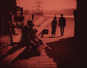 Movie still from “Intolerance” (1916), directed by D.W. Griffith – A man sitting on top of a bench next to a dock; Extreme Wide shot, High angle