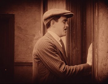 Movie still from “Intolerance” (1916), directed by D.W. Griffith – An old photo of a man wearing a hat and a suit; Medium shot, High angle