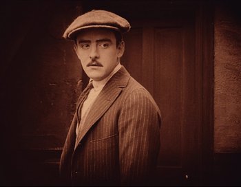 Movie still from “Intolerance” (1916), directed by D.W. Griffith – A man wearing a hat and a suit; Close Up shot, High angle