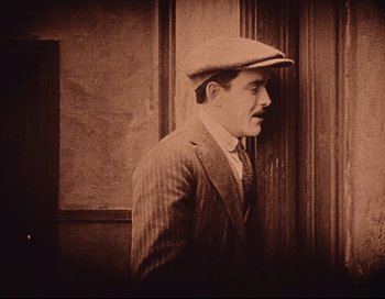 Movie still from “Intolerance” (1916), directed by D.W. Griffith – An old photo of a man in a suit and a hat; Medium shot, High angle